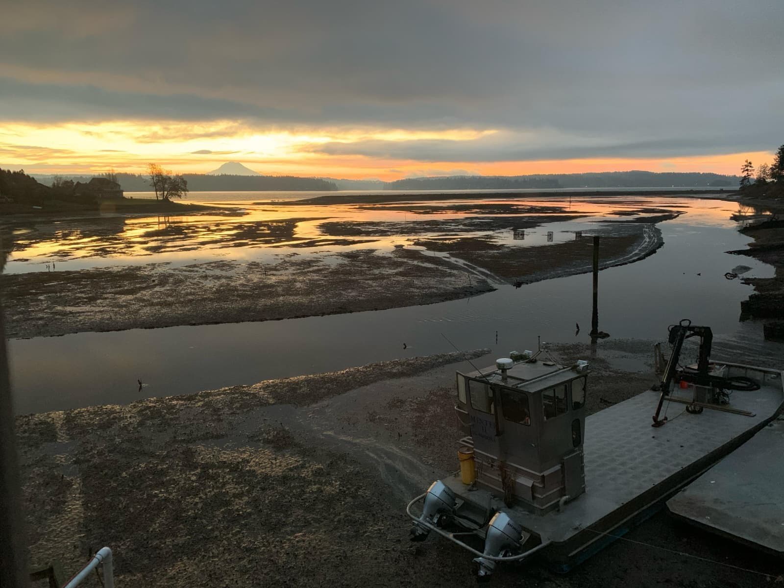 Low tide over the Minterbrook tidelands at sunrise, with a work barge on the shore and Mount Rainier on the horizon